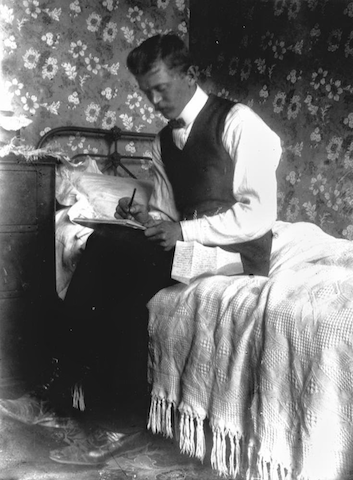 photograph of man sitting on bed writing